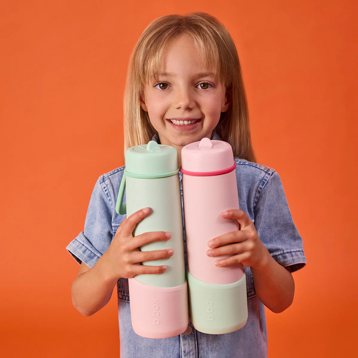 Child holding two colorful bottles against an orange background
