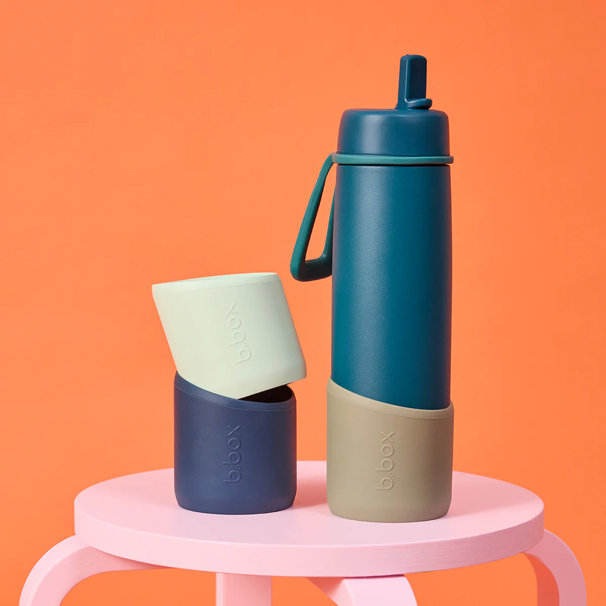 Two insulated drink containers on a pink stool against an orange background