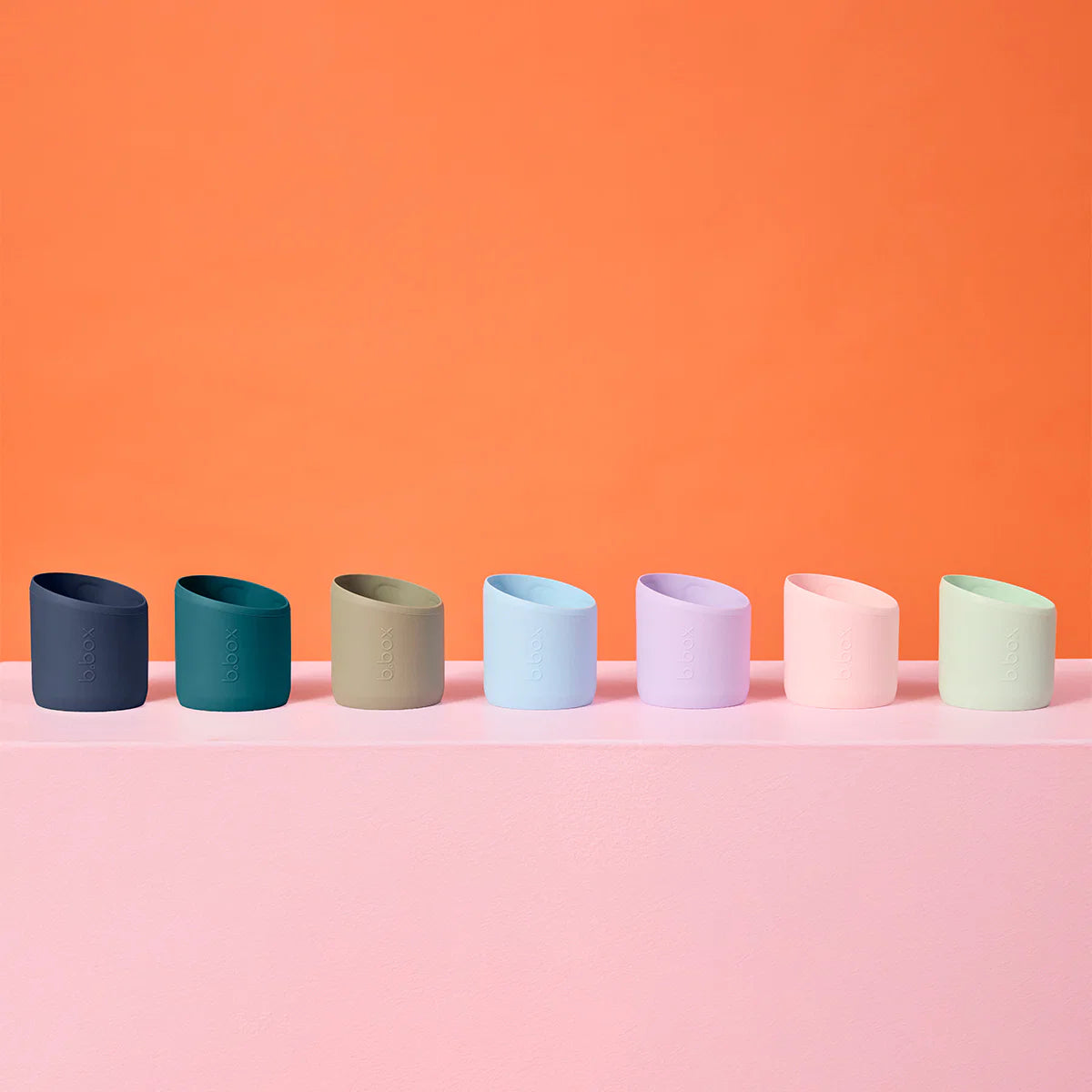Row of colorful cylindrical objects on a pink surface with an orange background