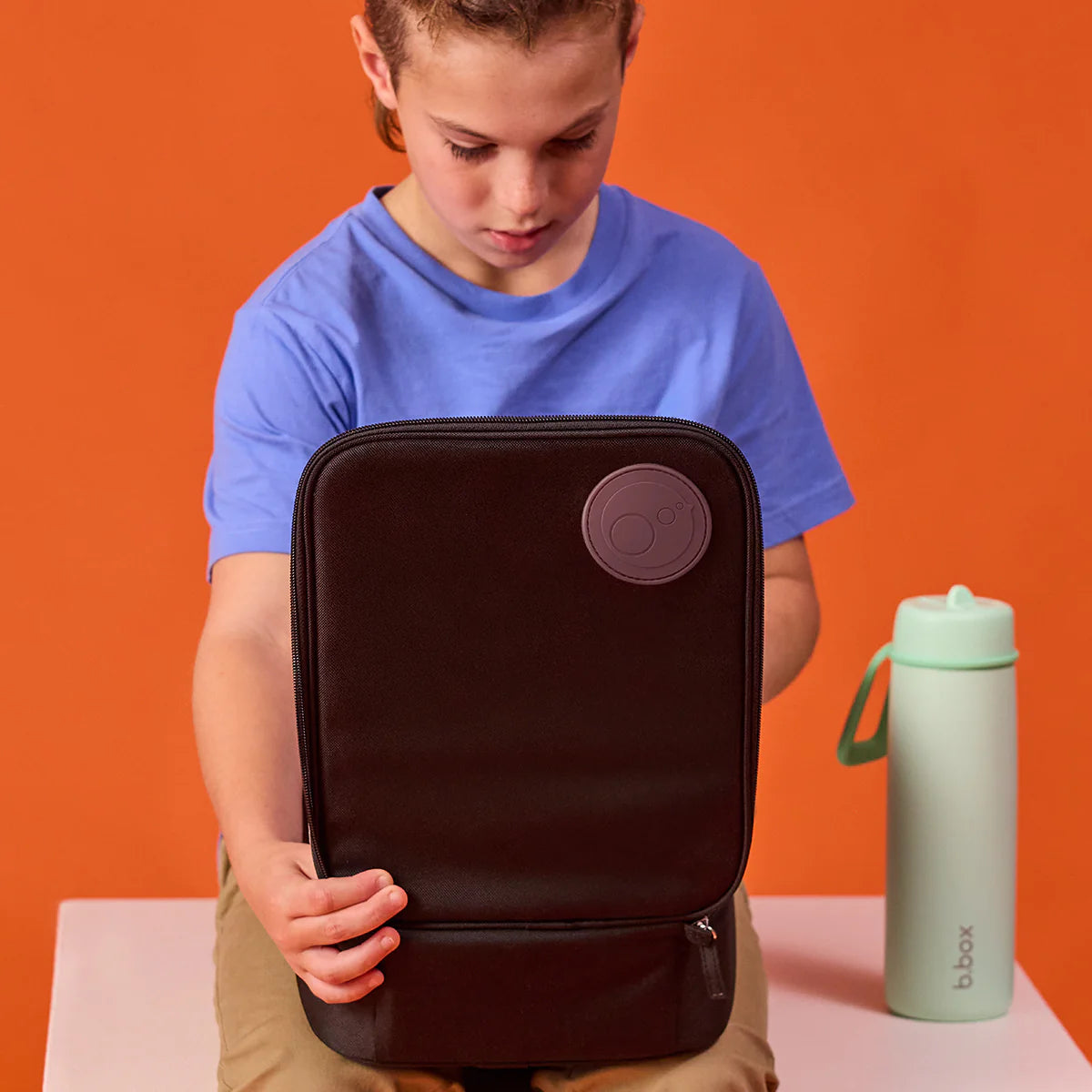 Child holding a black backpack with a purple circle on an orange background