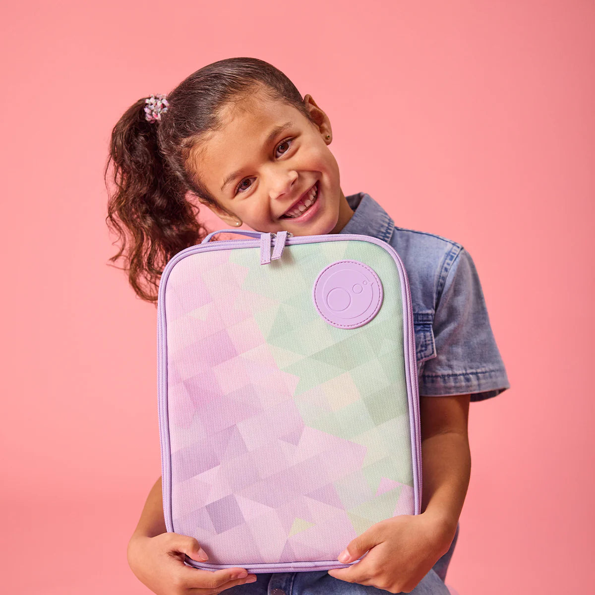 Child holding a pastel-colored case with a logo on a pink background