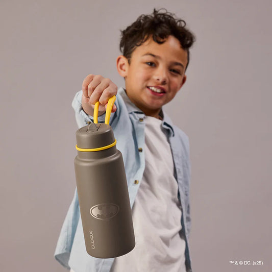 Child holding a brown water bottle with a yellow cap against a plain background