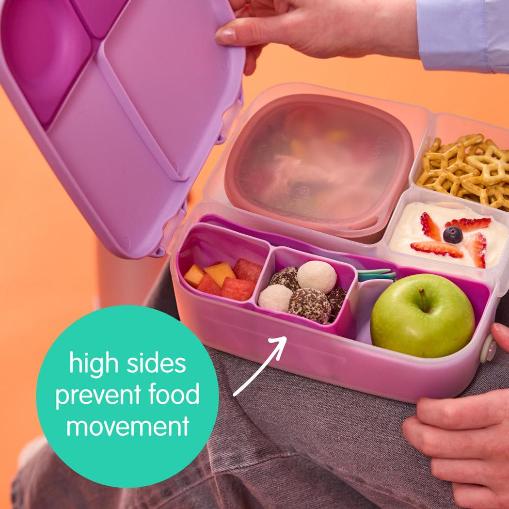 Pink bento box with compartments filled with food, held by a person, on an orange background.