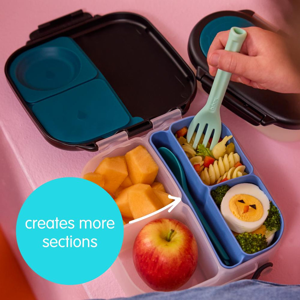 Bento box with compartments filled with food, including fruits and vegetables, on a pink background.
