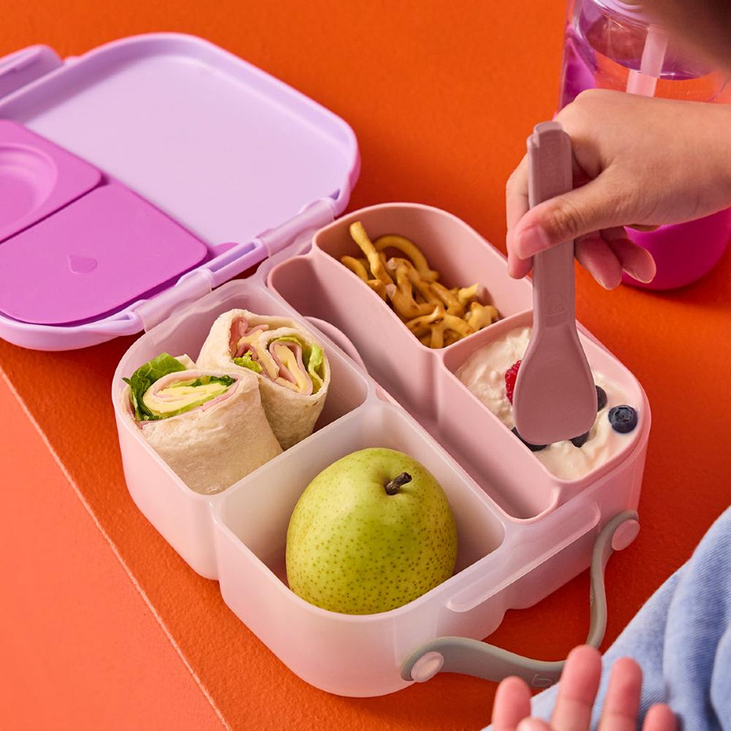 Pink bento box with compartments containing food on an orange background