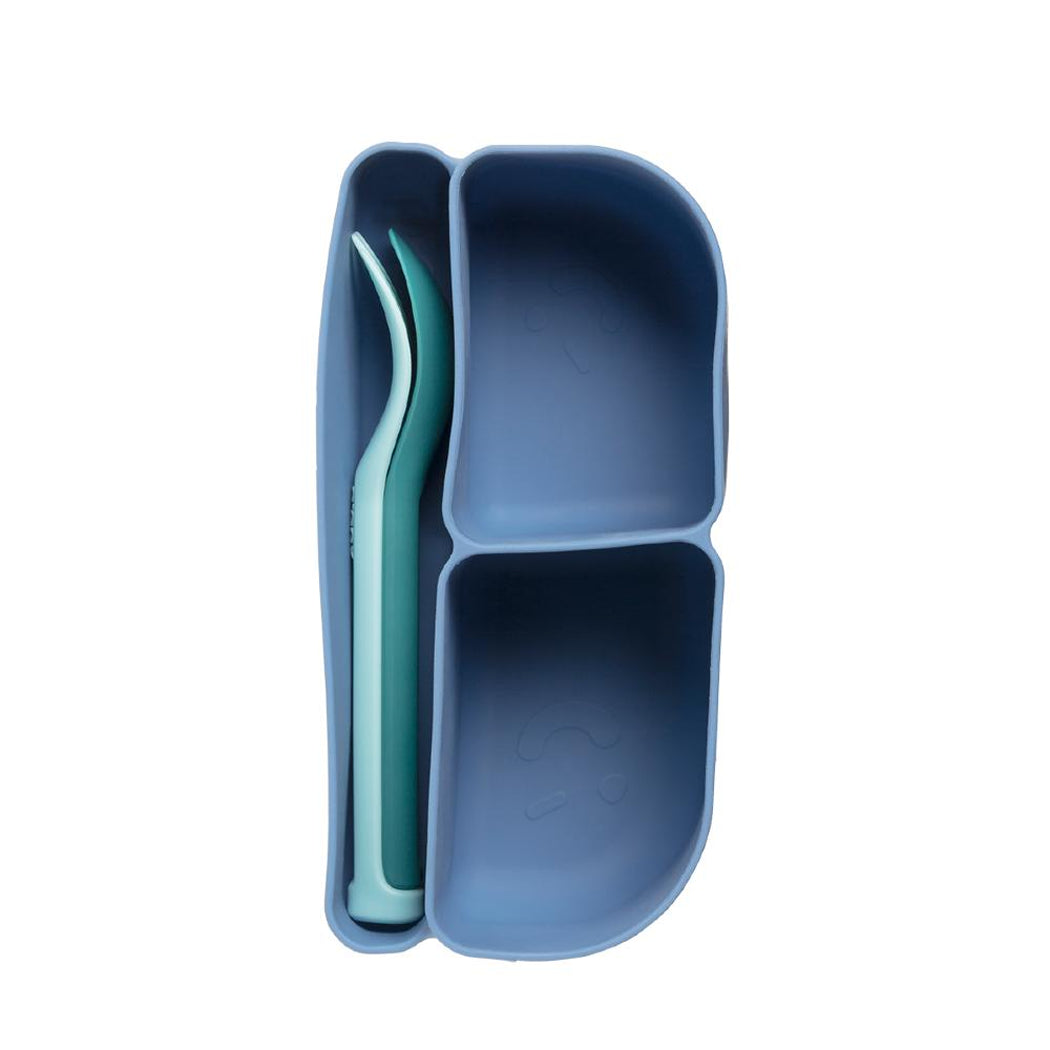 Blue divided plate with a green spoon on a white background