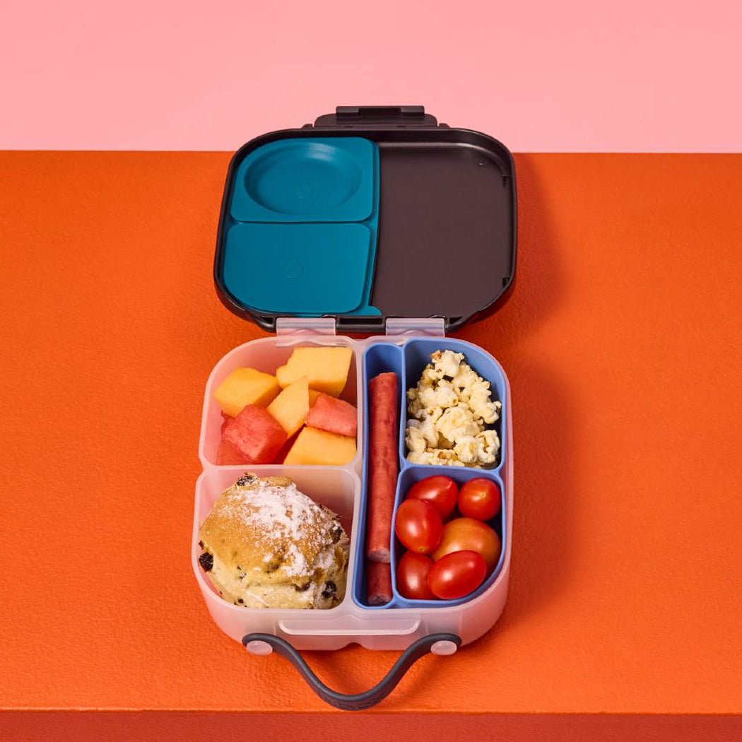 Open bento box with compartments of food on a pink and orange background