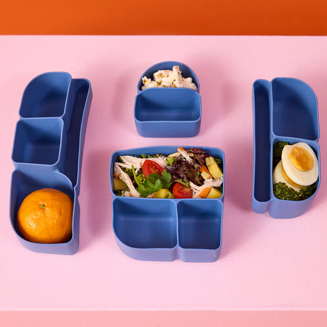 Blue bento box with compartments containing food on a pink background