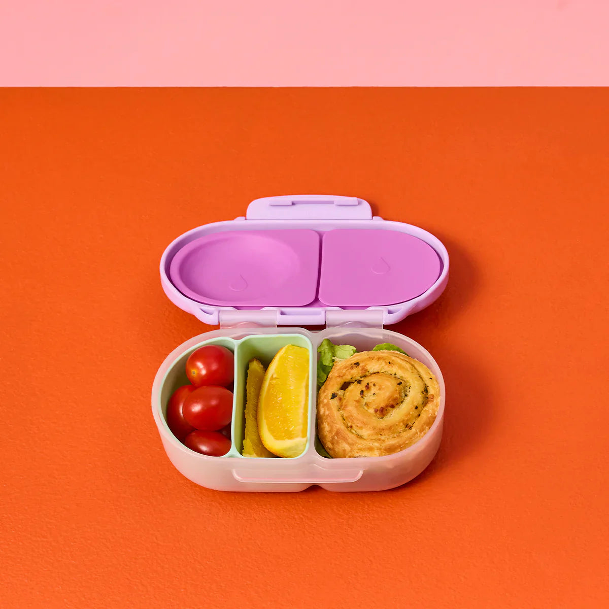 Pink bento box with compartments containing food on an orange background