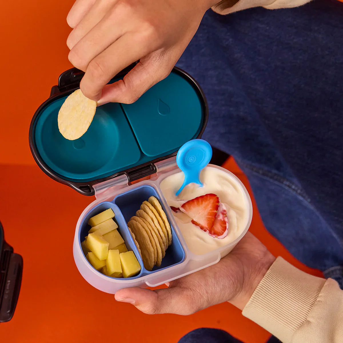 Hands opening a bento-style lunch box with compartments containing snacks.