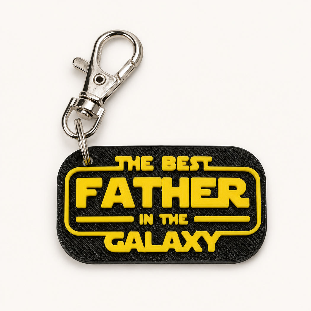 A black rectangular keychain with rounded corners featuring the yellow text 'THE BEST FATHER IN THE GALAXY' in a Star Wars-style font, attached to a silver metal lobster clasp, on a clean white background.