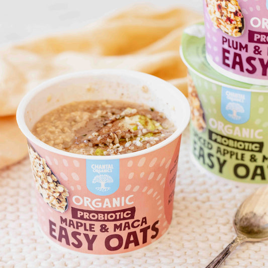 Container of Organic Probiotic Maple & Maca Easy Oats with a spoon and more containers in the background.