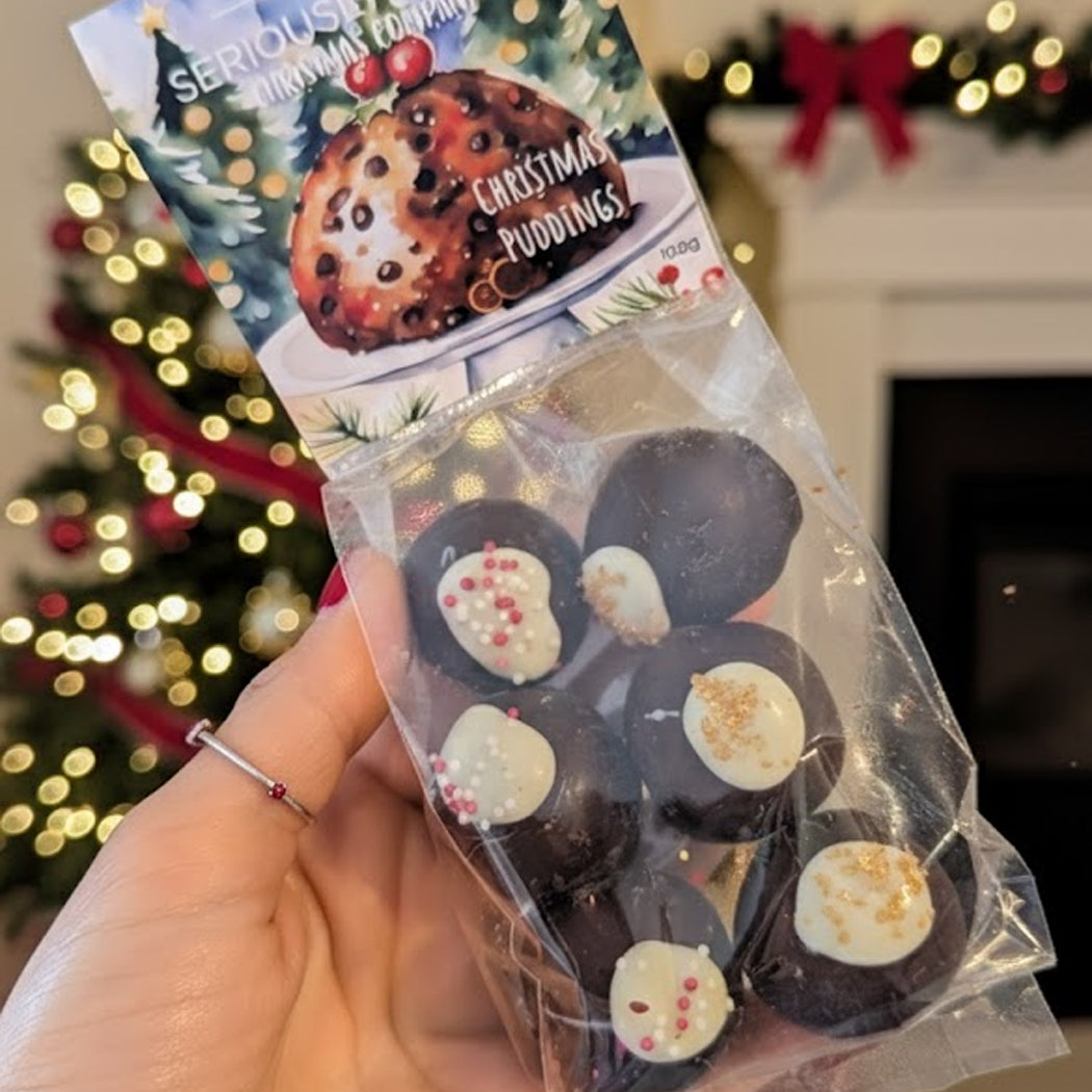 Packaged Christmas pudding cookies held in front of a decorated Christmas tree.