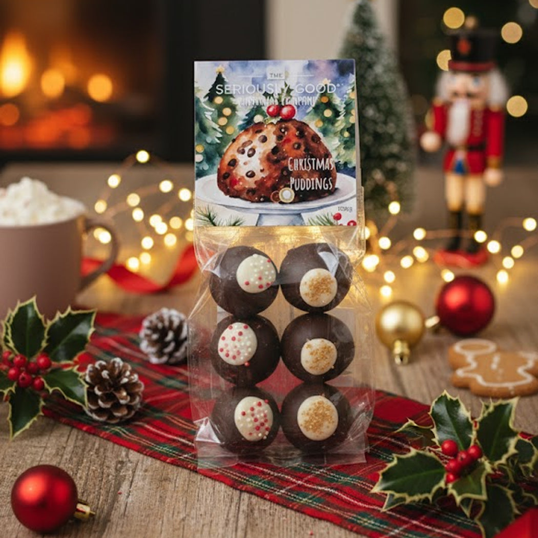 Packaged Christmas pudding truffles with festive decorations and a fireplace in the background
