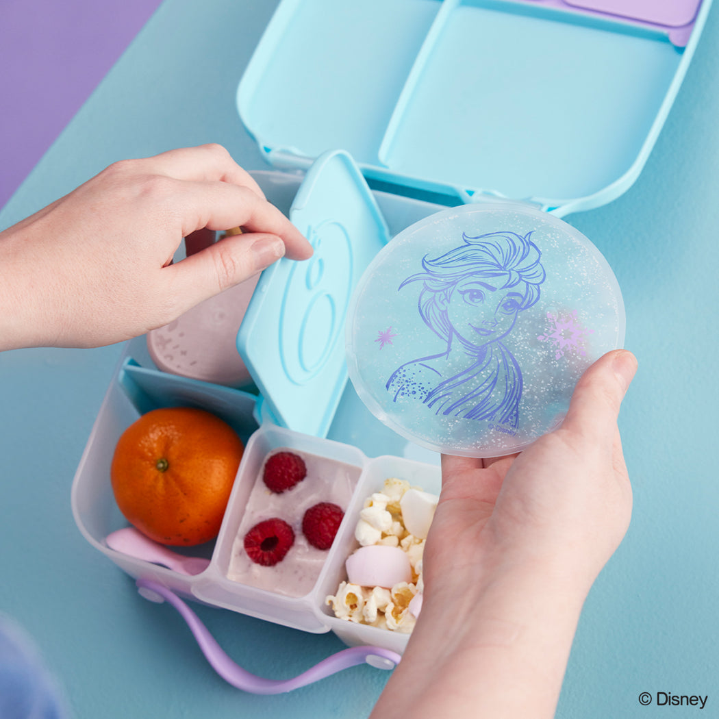 Bento box with snacks and a round container with a mermaid design on a blue background