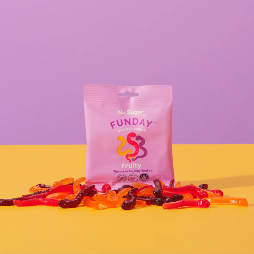 Pink bag of 'Funday' gummy worms on a yellow surface with a purple background