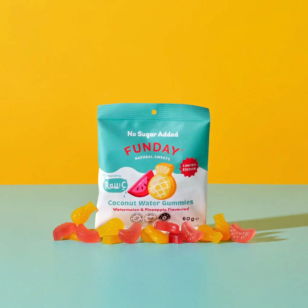 A bag of Funday Coconut Water Gummies (watermelon and pineapple flavored) sits on a light blue surface against a bright yellow background, with several loose gummy candies scattered in front of the package.
