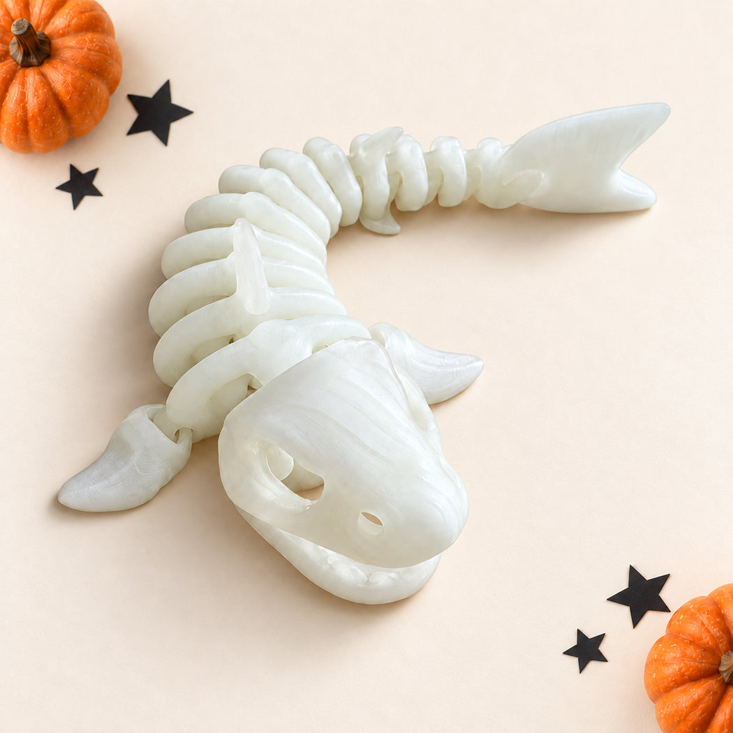 A white skeleton shark toy or decorative sculpture shown on a light beige background with small orange pumpkins and black star cutouts as props.