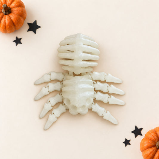 An off-white bone-colored spider decoration styled on a light beige background with small orange pumpkins and black star cutouts.