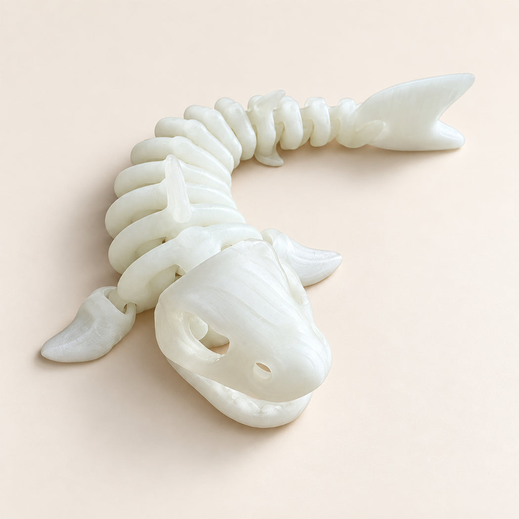 A 3D-printed articulated shark skeleton toy in off-white, shown on a solid pale peach background.