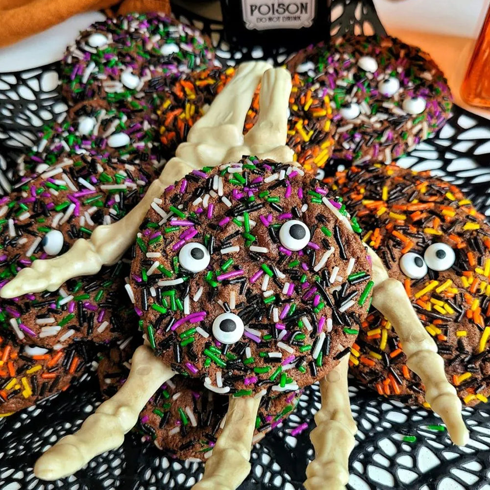 Halloween-themed cookies shaped like spiders with colorful sprinkles and candy eyes on a black spider web plate.