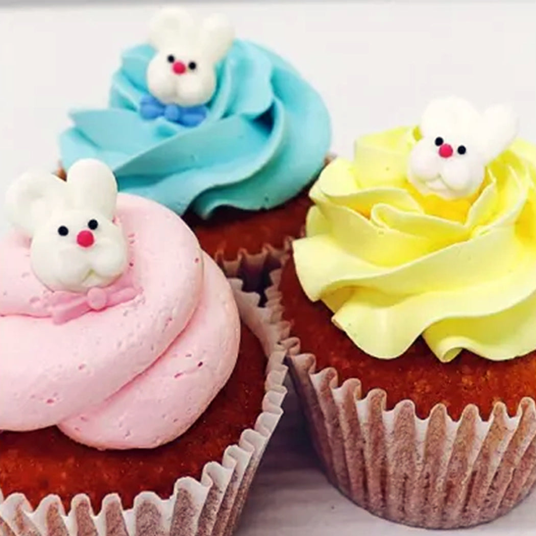 Three cupcakes with colorful frosting and bunny decorations on a white background