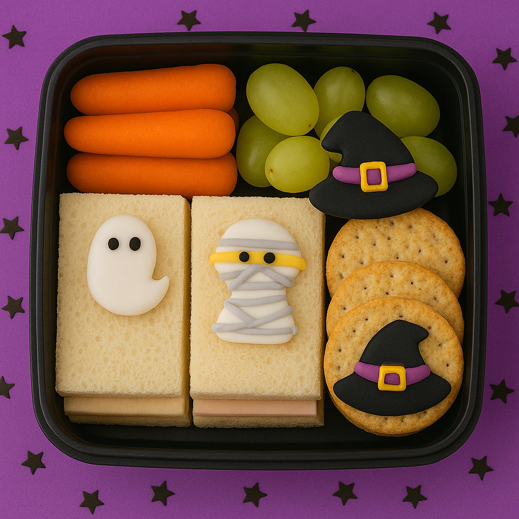 Halloween-themed snack tray with ghost and mummy cookies, carrots, grapes, and witch hats on a purple background.