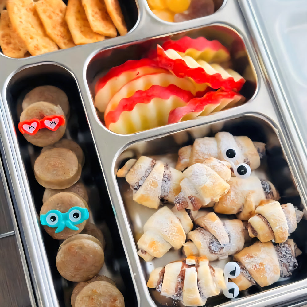 Metal bento box with various snacks including cookies, fruit slices, and wrapped snacks.