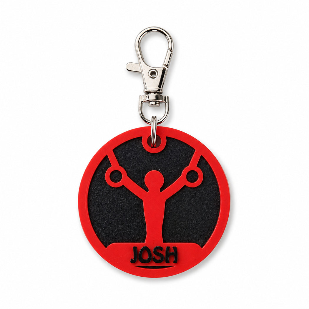 A circular red and black keychain tag featuring a gymnast silhouette with the name 'JOSH' at the bottom, attached to a silver swivel clasp on a white background.