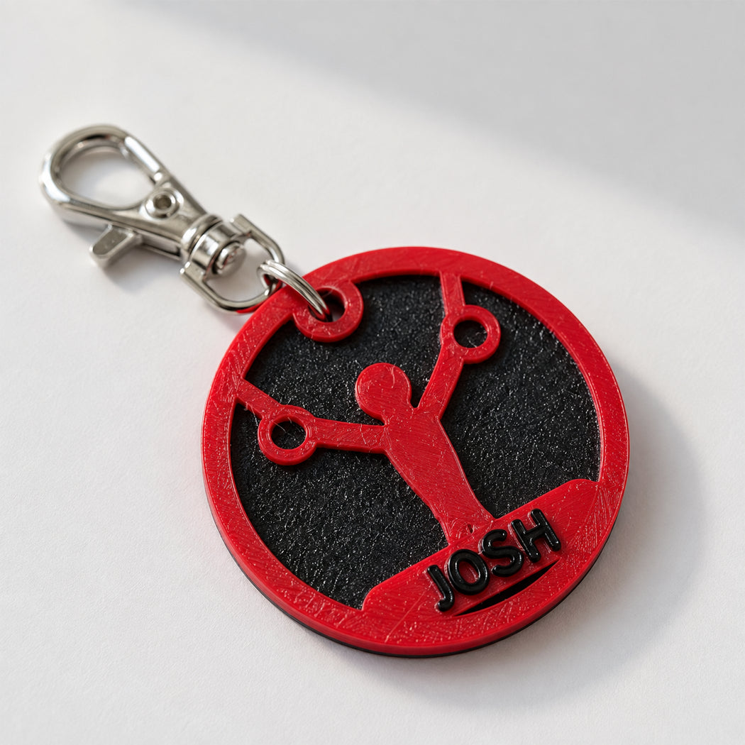 A custom circular red and black keychain tag featuring a basketball player silhouette and the name 'JOSH', attached to a silver metal clasp on a light gray background.