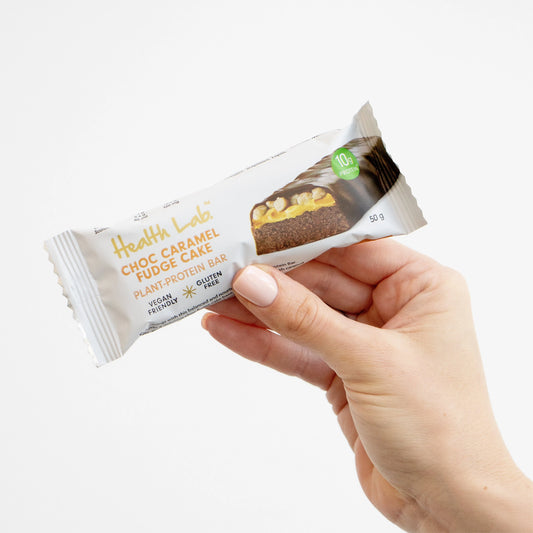 Hand holding a 'Health Label' Choc Caramel Fudge Cake protein bar against a white background