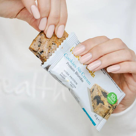 Protein bar with 'Cookies & Cream' flavor packaging held by hands against a white background