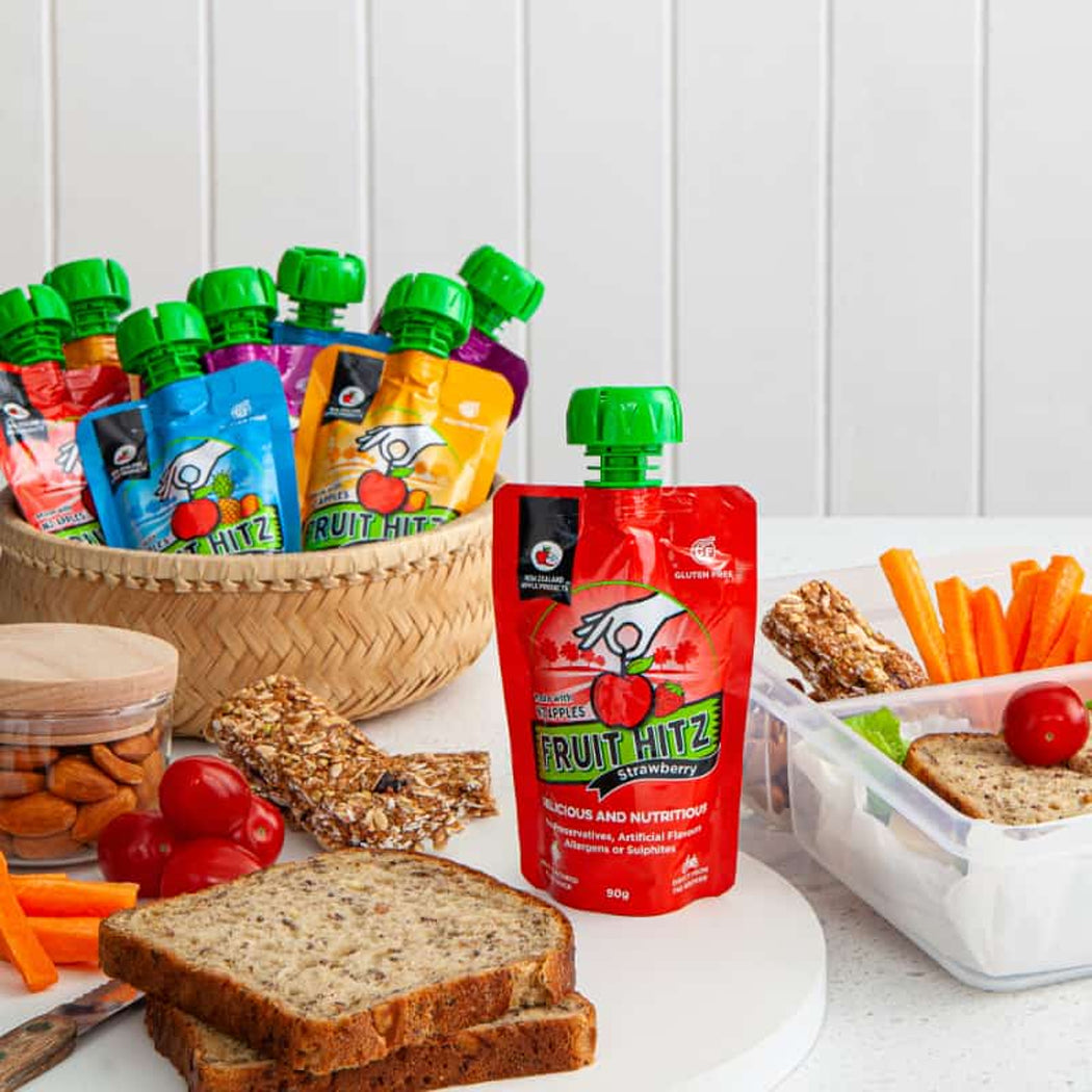 Assorted snacks including fruit pouches, bread, and vegetables on a white surface.