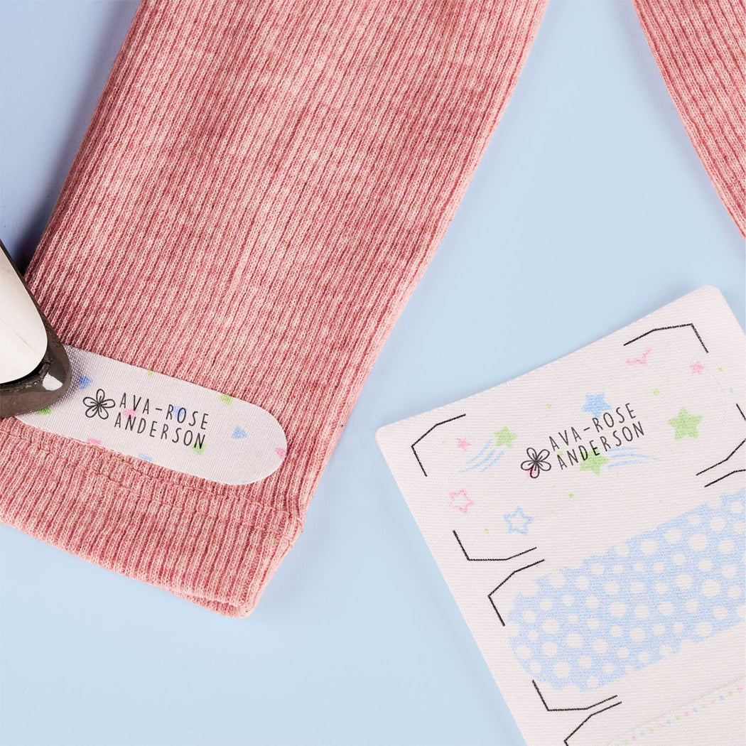 A close-up of a pink ribbed knit sleeve or cuff with a printed personalized label reading 'AVA-ROSE ANDERSON,' placed on a light blue background with part of a matching printed card visible.