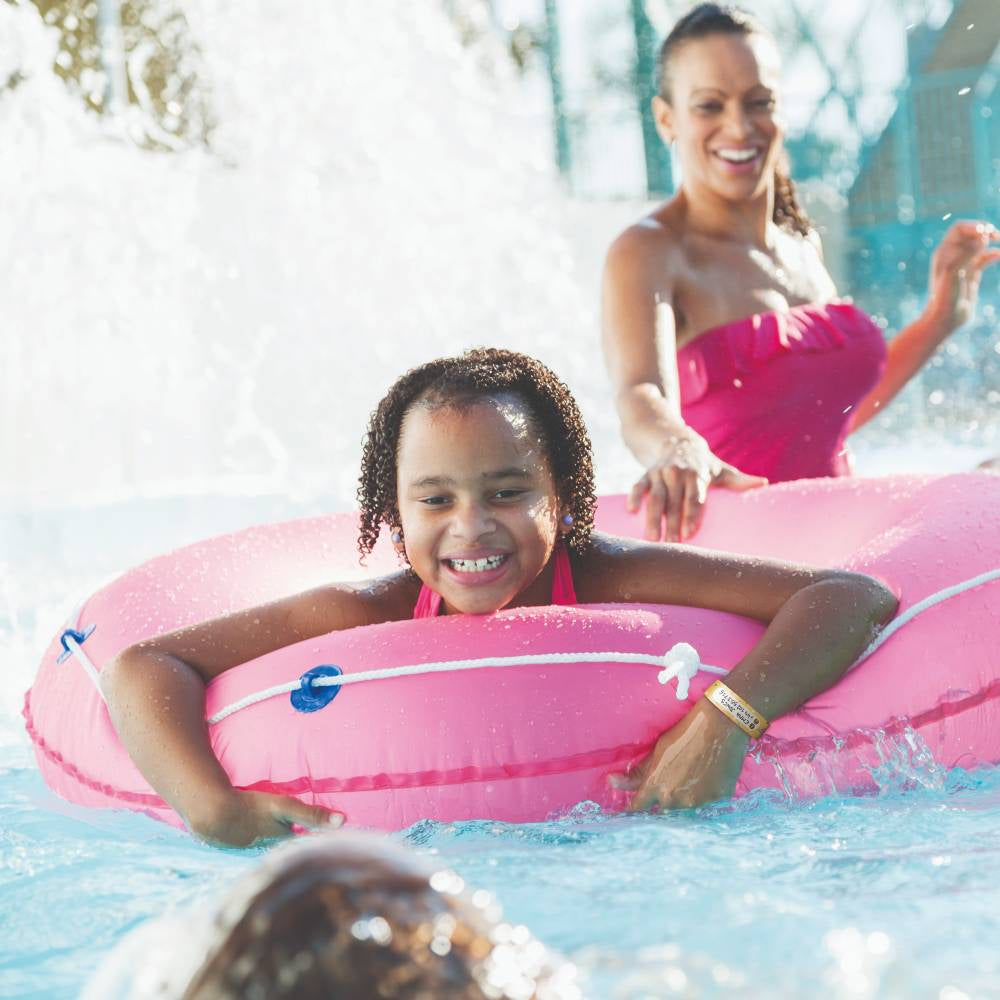 Girl on a pink inflatable ring in a pool with a woman in the background