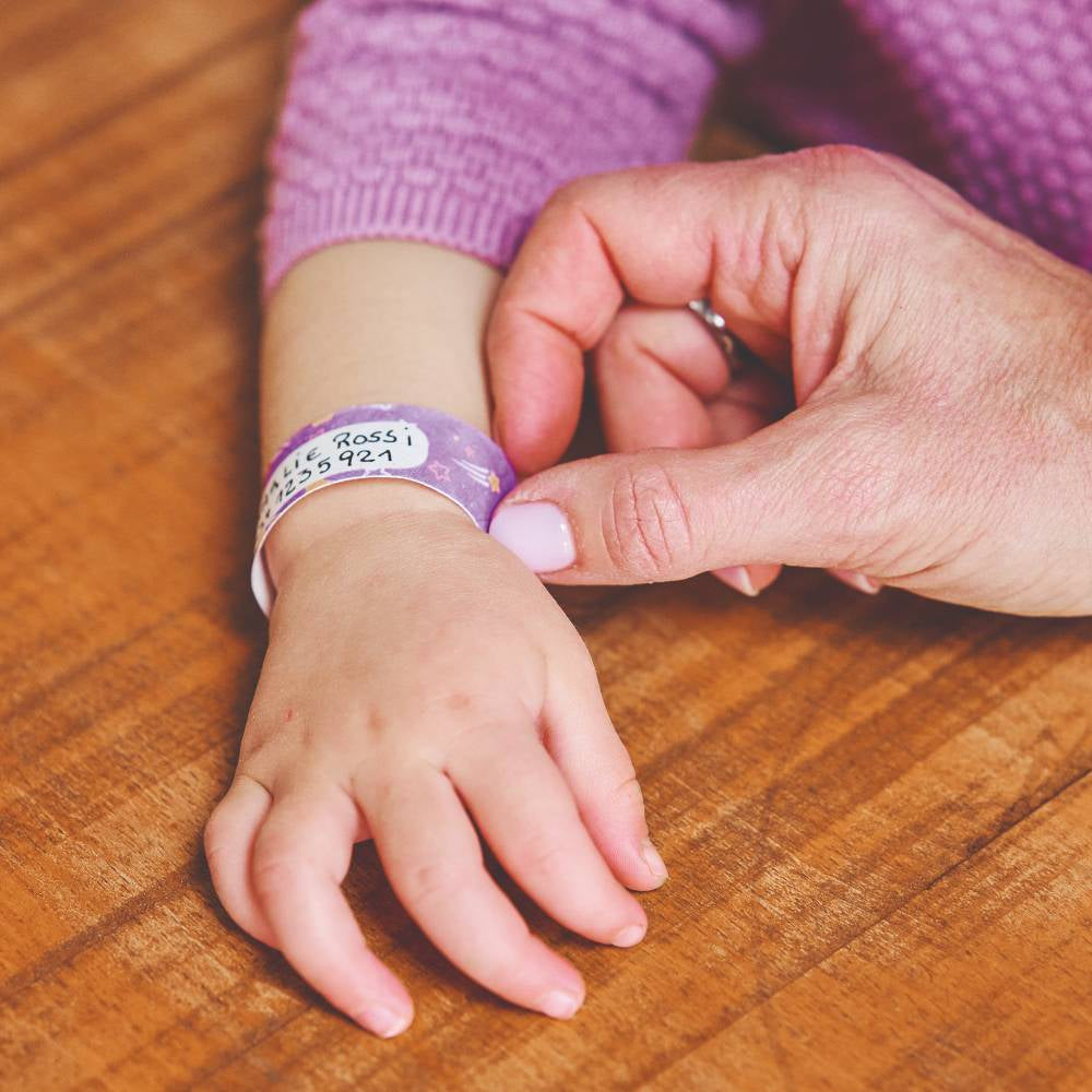Person placing a purple wristband with text on a child's wrist on a wooden surface