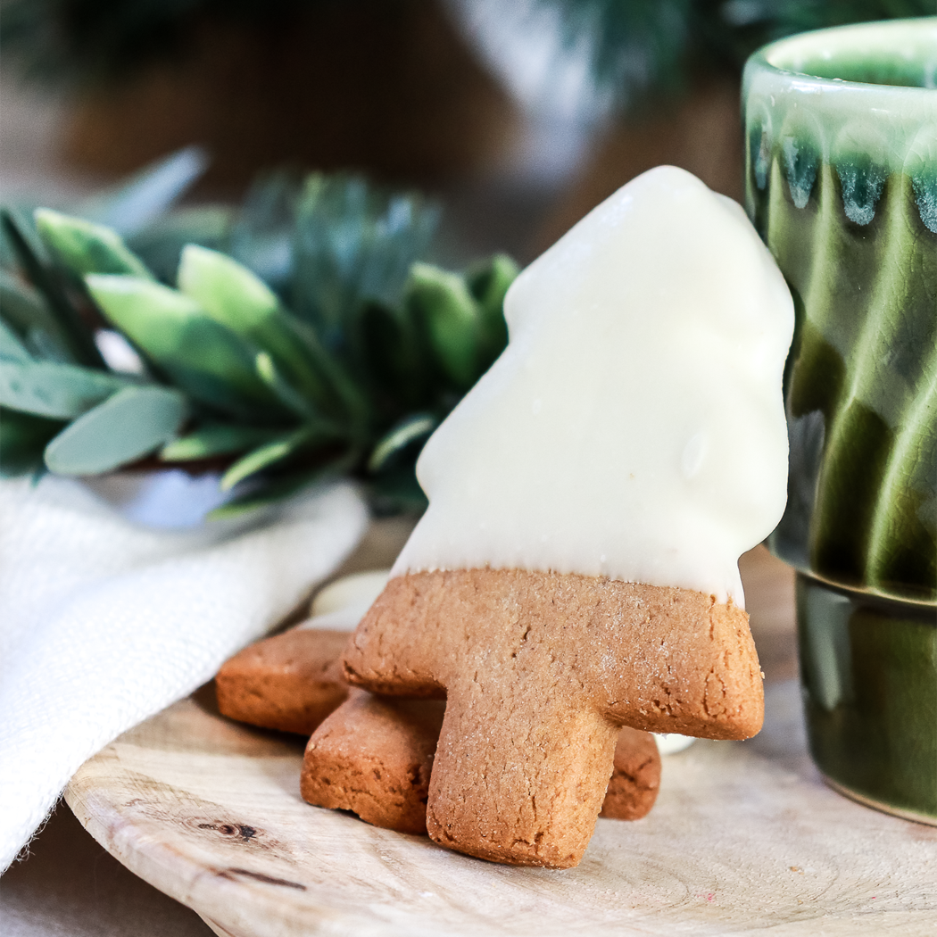 Tree-shaped cookie with white icing on a wooden board with a green mug in the background.