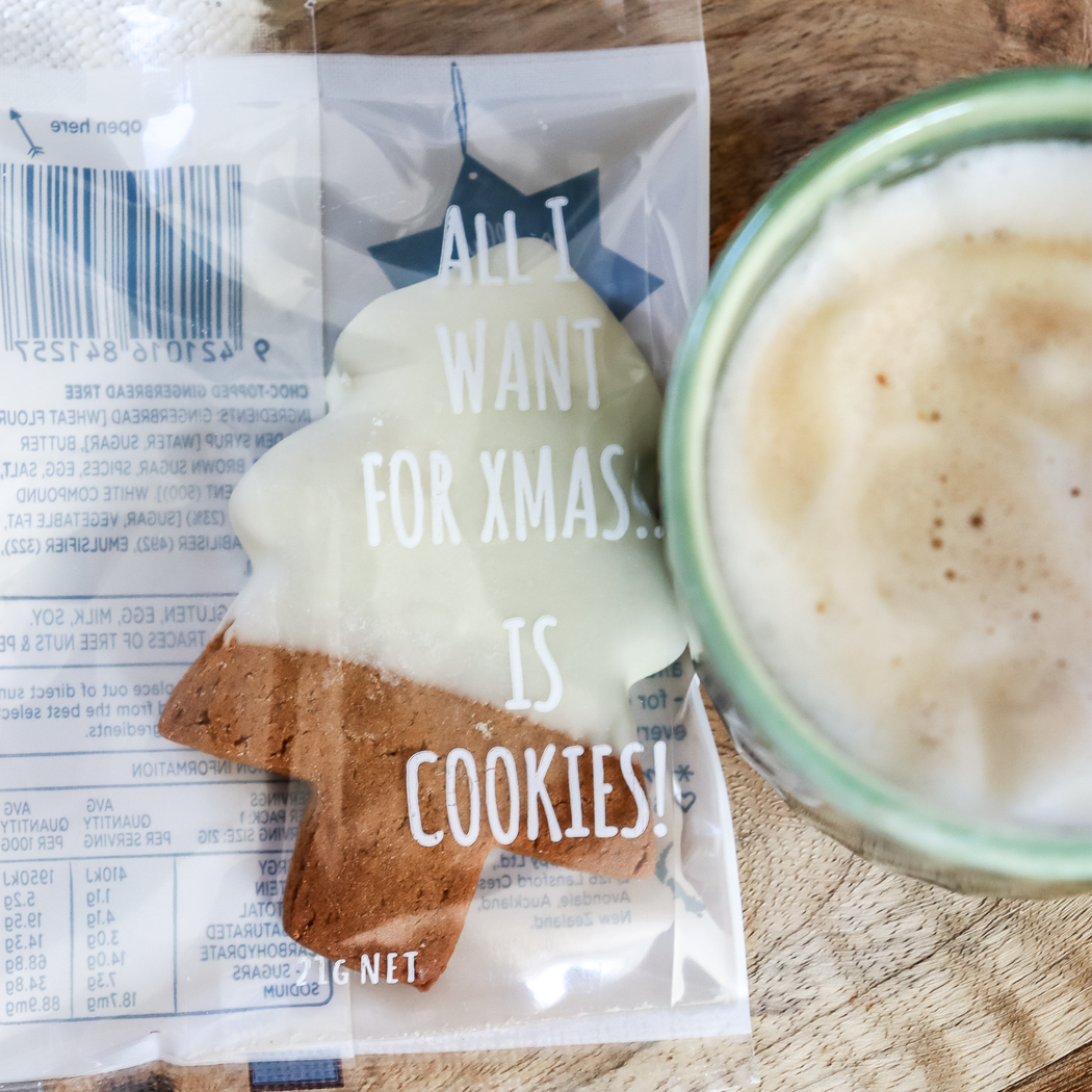 Cookie with 'All I want for Xmas is cookies!' text on packaging next to a cup of coffee.