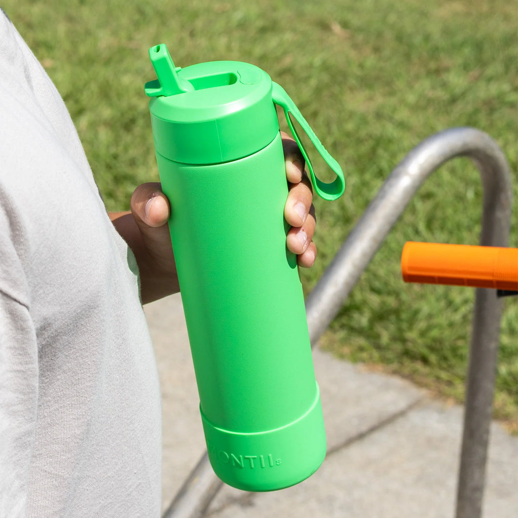 Person holding a green water bottle with a grassy background