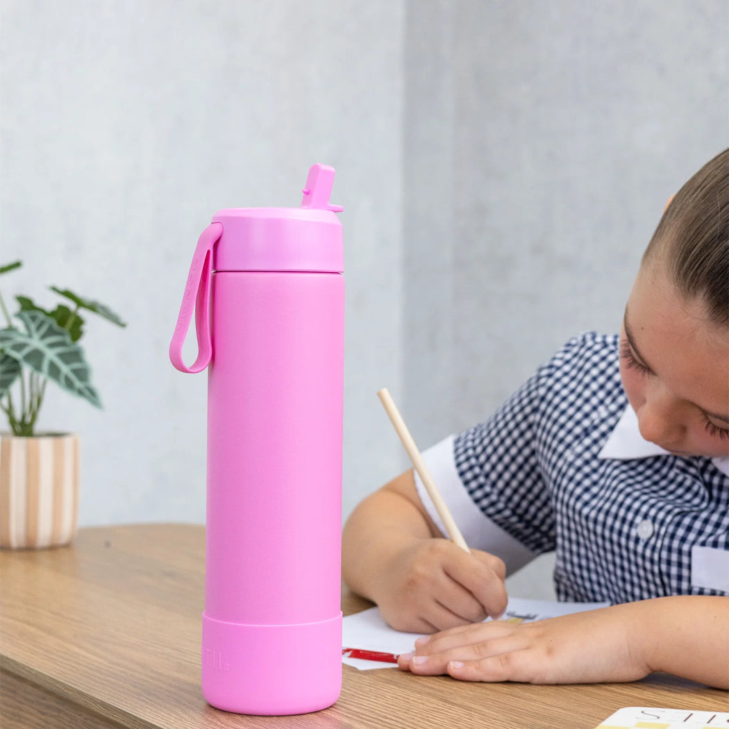 Pink water bottle on a table with a child writing in the background