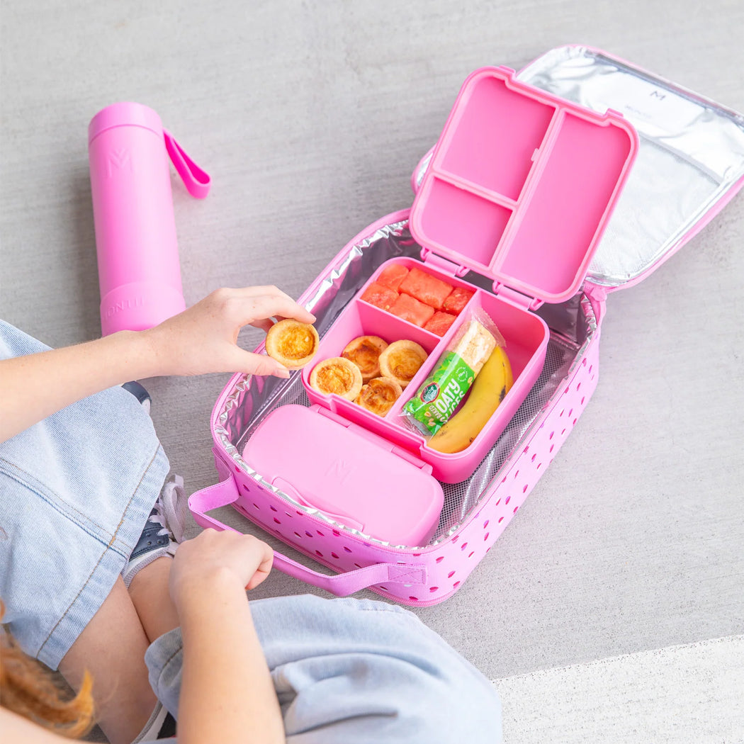 Pink bento box with compartments containing snacks, next to a pink water bottle on a gray surface.