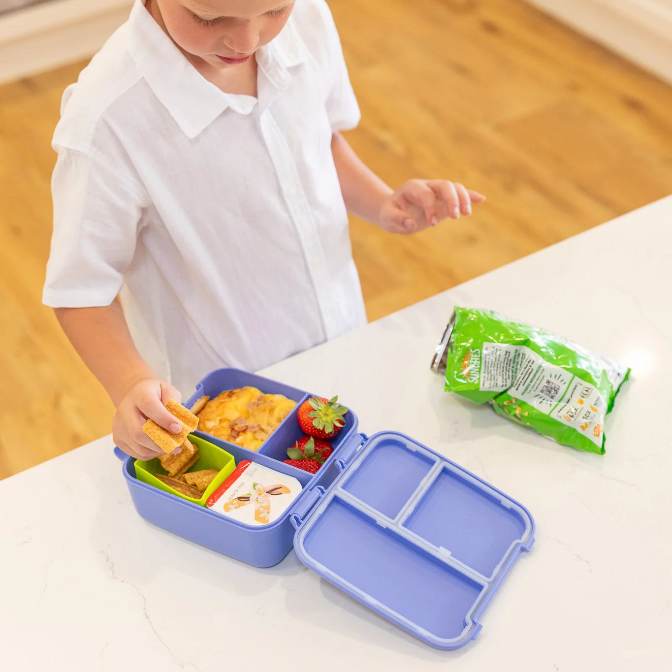 Child opening a blue bento box with compartments on a wooden floor.