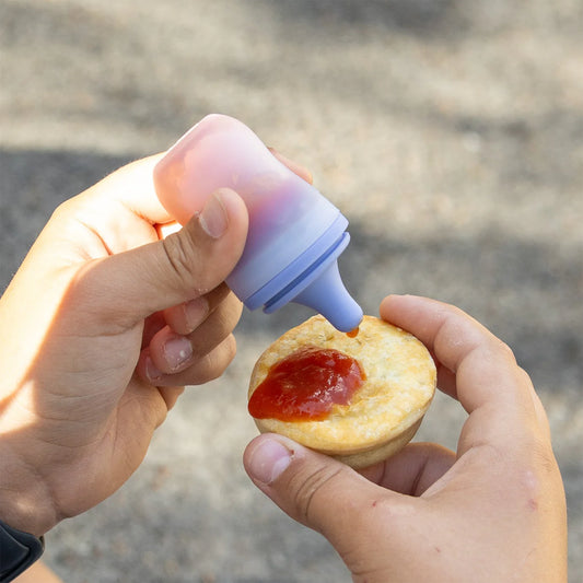 Person applying red sauce from a small bottle onto a pastry.