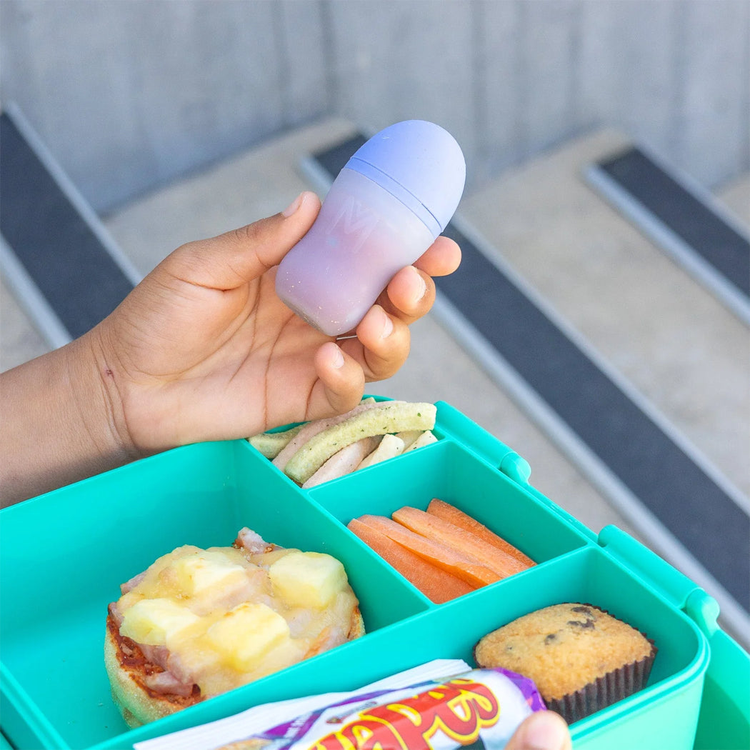 Hand holding a purple container over a teal bento box with food