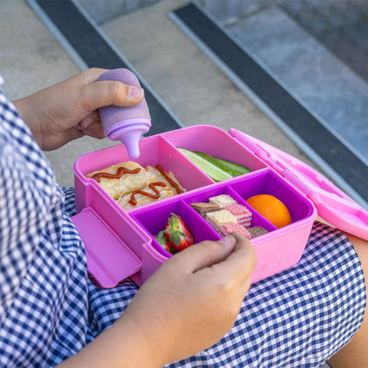 Person preparing a lunchbox with compartments filled with food, sitting on steps.