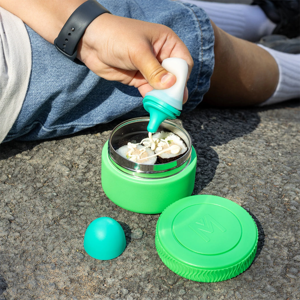 Person using a green and white container with a lid on a concrete surface