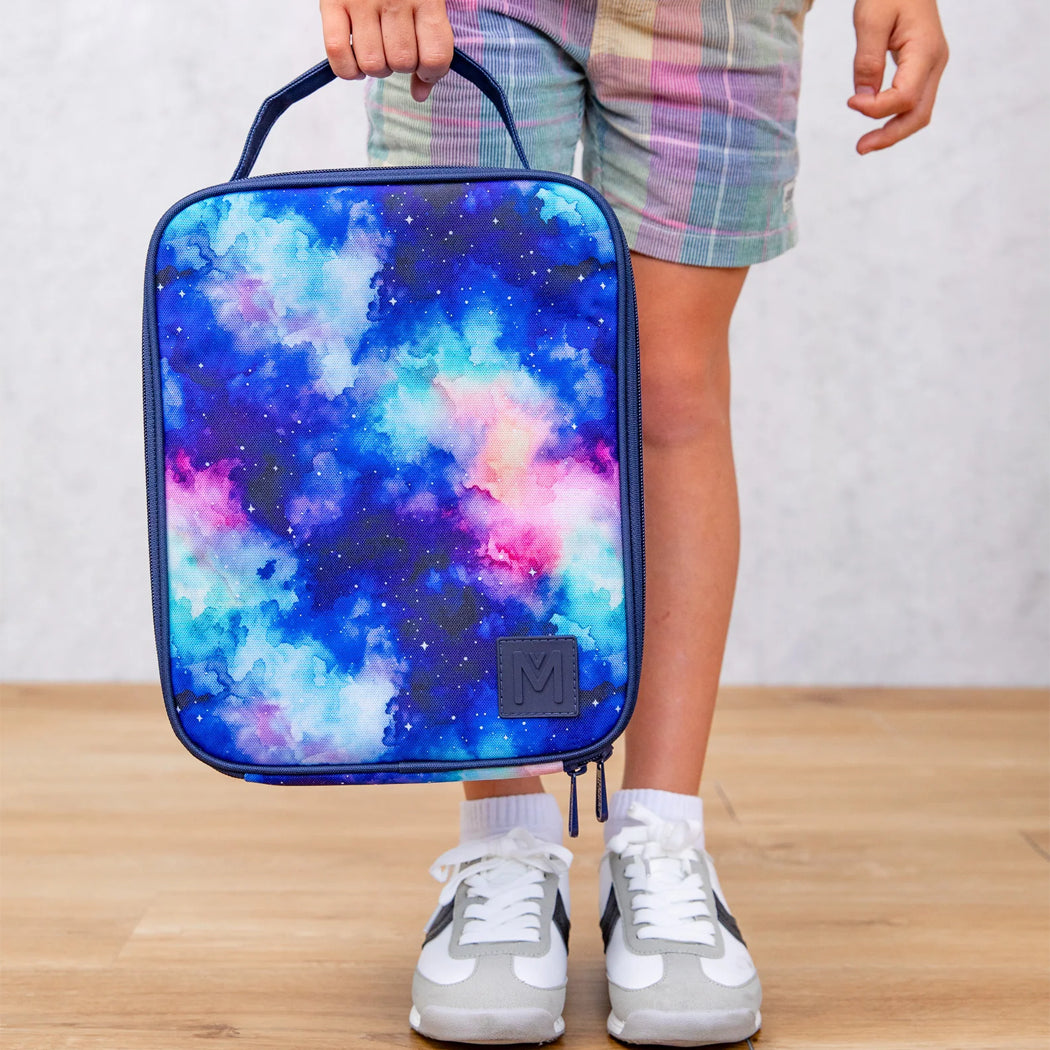Person holding a colorful backpack with a starry night design on a wooden floor.