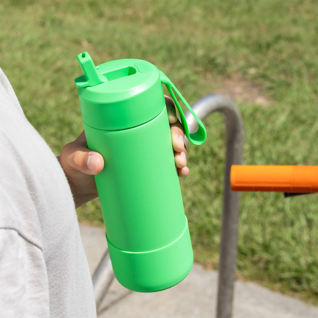 Person holding a green water bottle outdoors with grass in the background