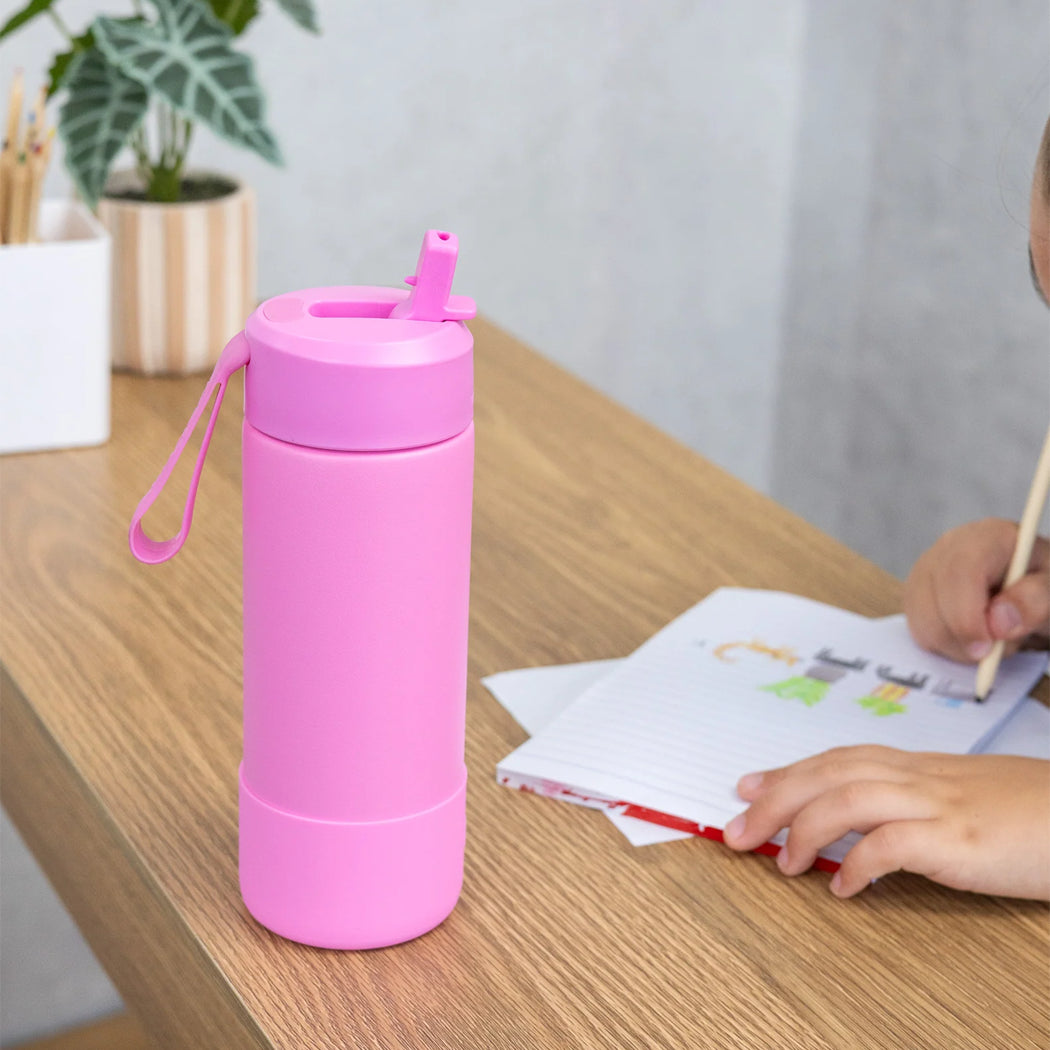 Pink water bottle with a straw on a table next to a child writing.
