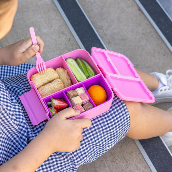 Child holding a pink bento box with various food items and a fork.